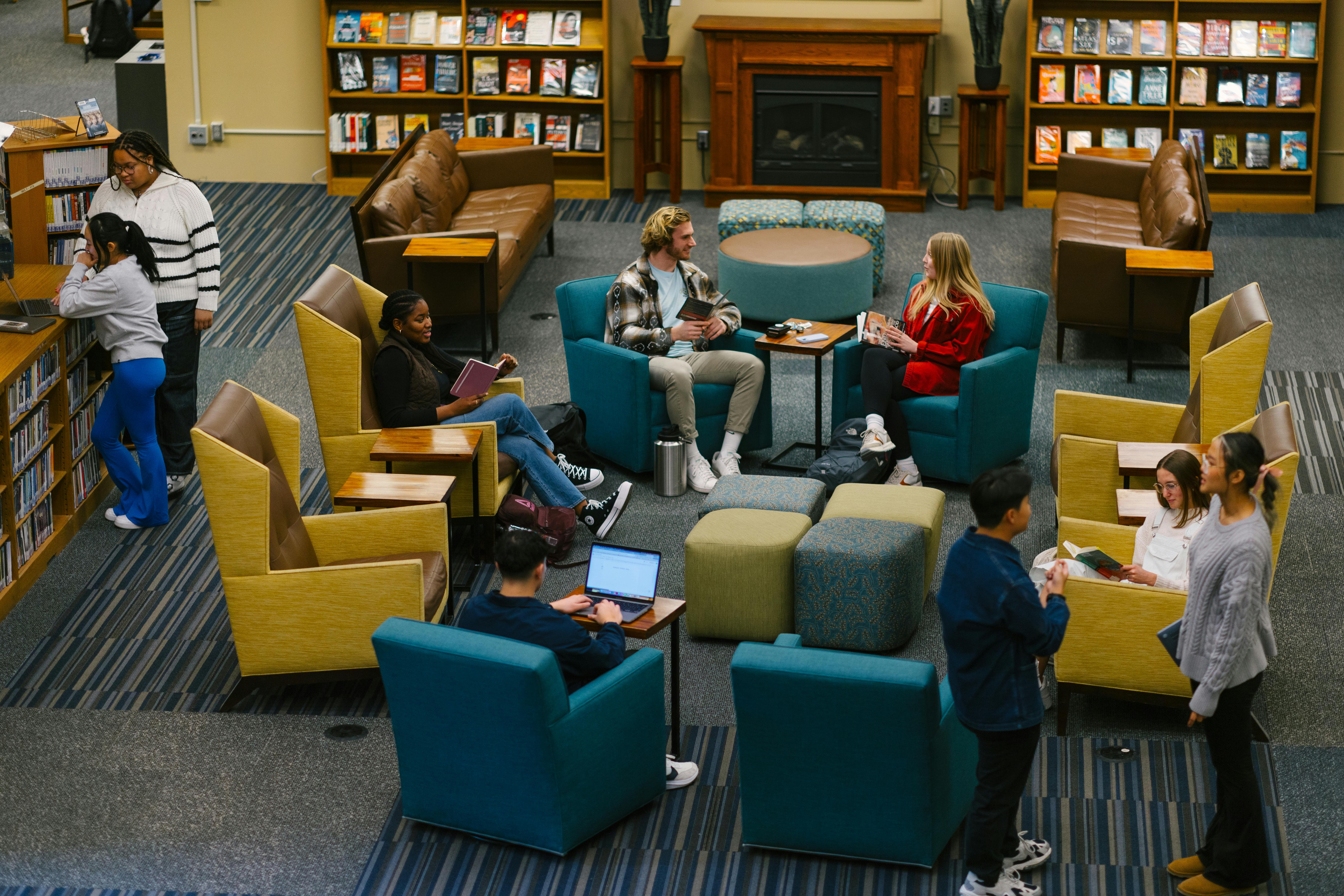 Students in the library, using the chairs, tables, and aisles.