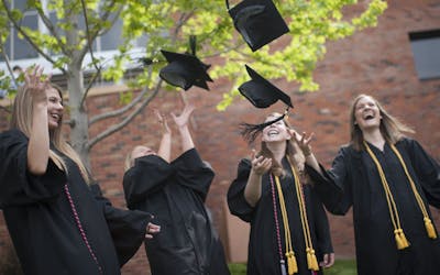 Undergrad students in graduation gowns toss their caps.
