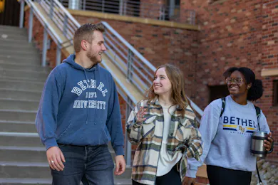 three students smiling, walking outside