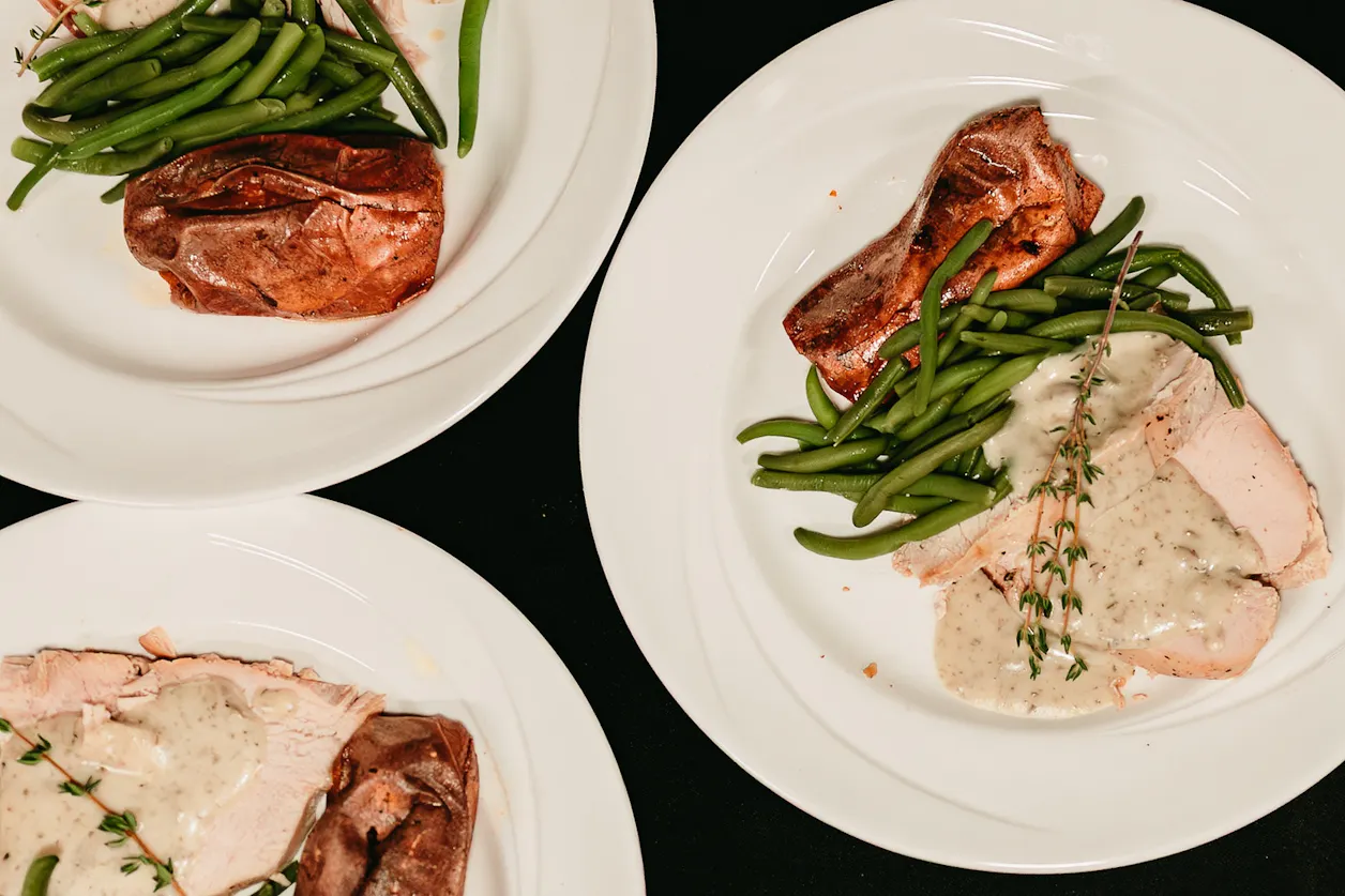 Plates of sliced meat, green beans, and potatoes with sauce.