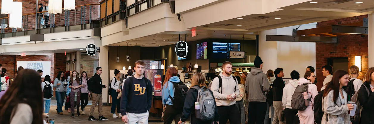 Students gather near dining counters in a busy campus dining hall.
