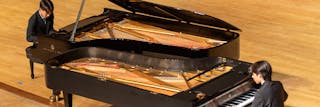 two students playing a duet on two pianos