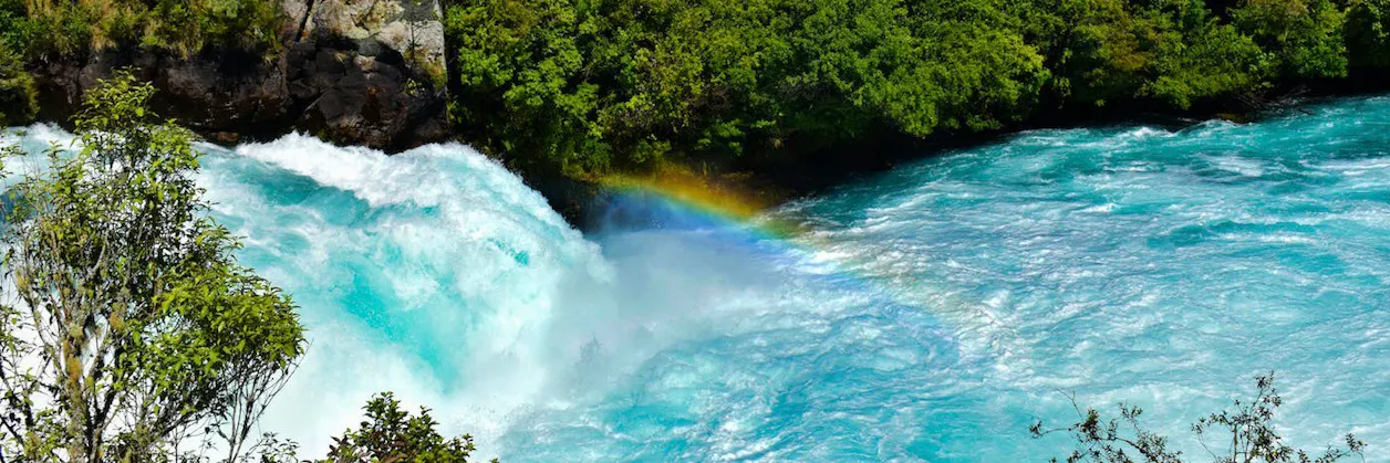 Clear blue rushing waters with a rainbow in the forest.