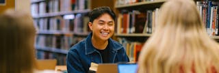 Smiling student sits with other students in the Bethel library.