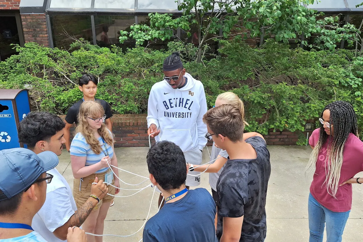 Students huddle in a group holding ropes outside as part of a group project. 