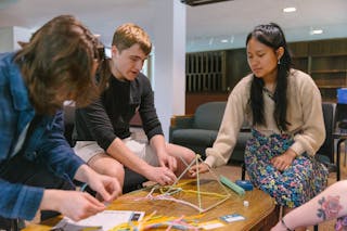 Students collaboratively building a structure with colorful craft materials at a table in a relaxed study area.