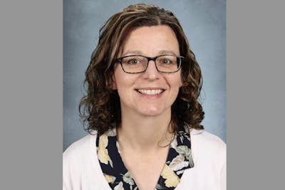Smiling woman with curly brown hair, wearing glasses and a floral blouse with a light cardigan.