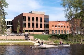 Bethel students sit on a dock stretching out into a lack before brick Bethel buildings. 