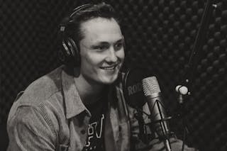 Bethel student Adam Bricker '25 sits in a podcast studio surrounded by podcast equipment.