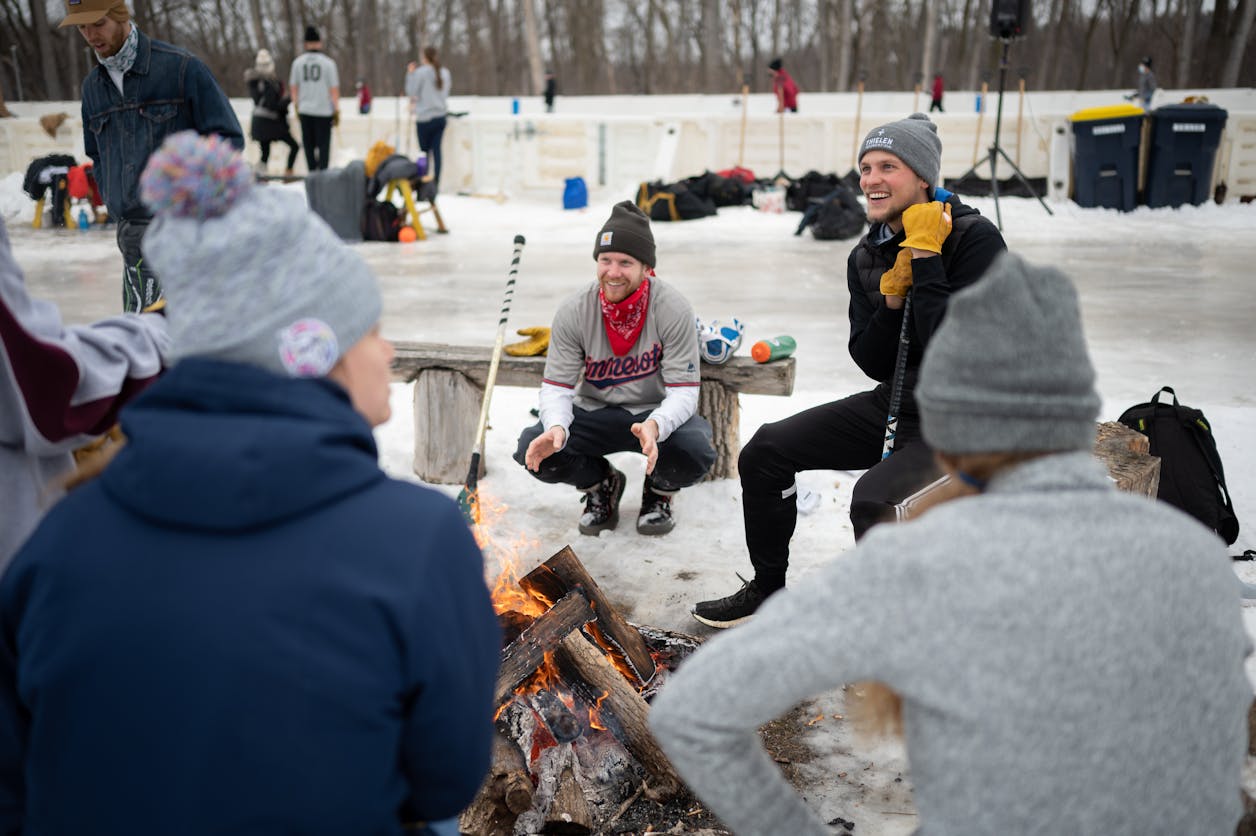Alumni gather around a fire next to a broomball rink at Bethel University