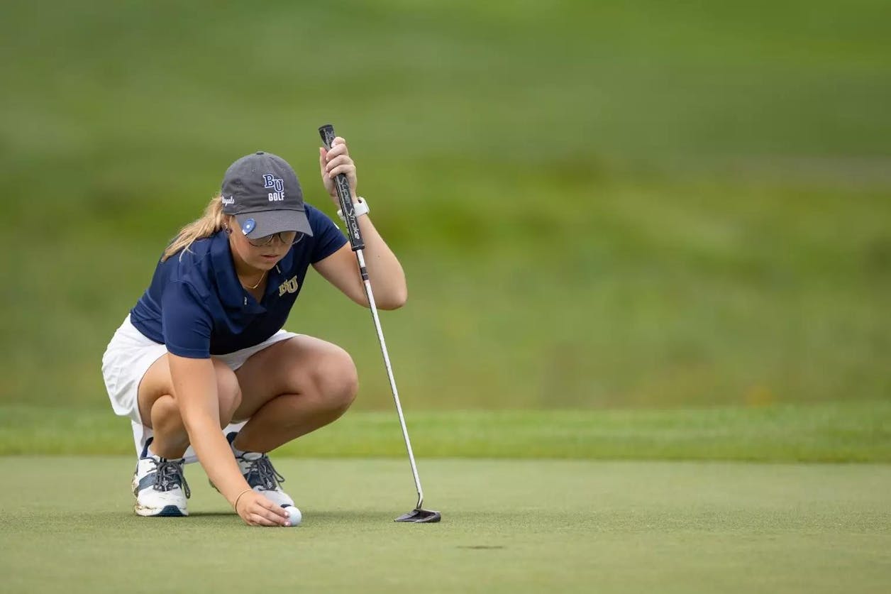 Bethel golfer lines up a putt, crouched on the green during a sunny round.