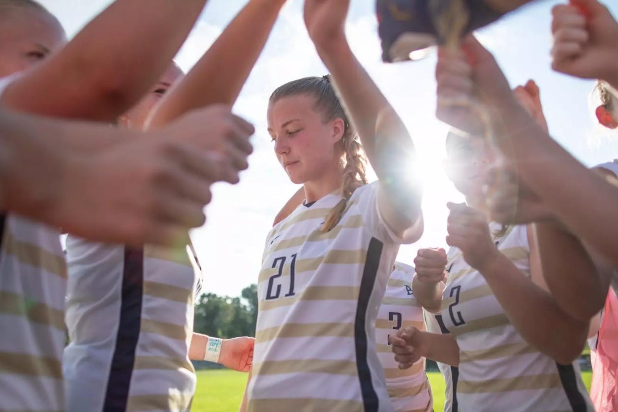 Bethel women’s soccer team forms a tunnel in a pregame tradition with sunlight shining through.