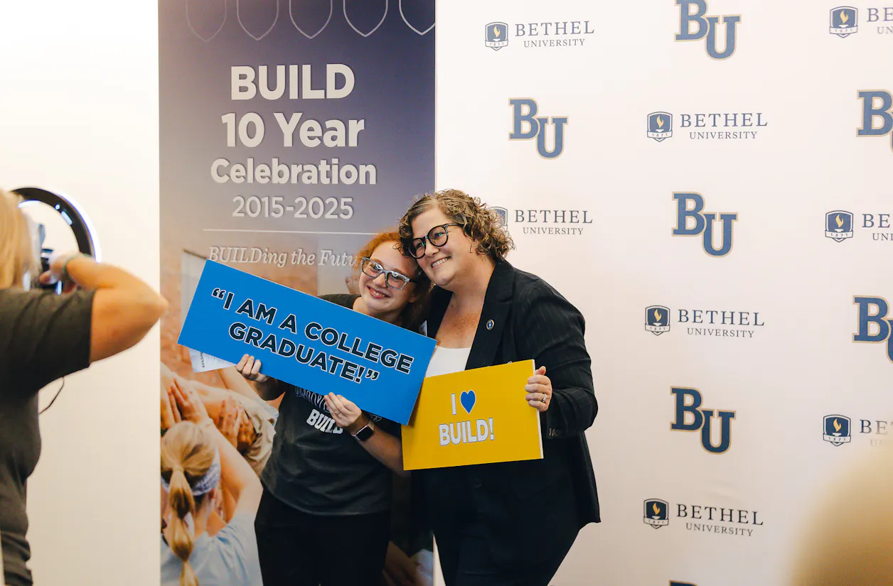 Two people smile holding BUILD signs at the BUILD 10-year celebration photo booth.
