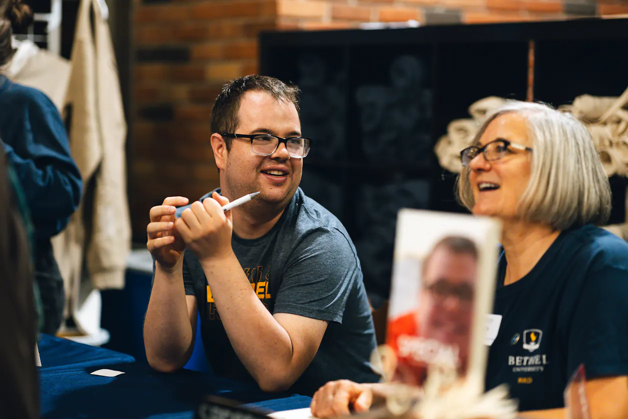 A student and his mom smile while working a table at the BUILDing the Future: 10 Years of Impact event at Bethel.