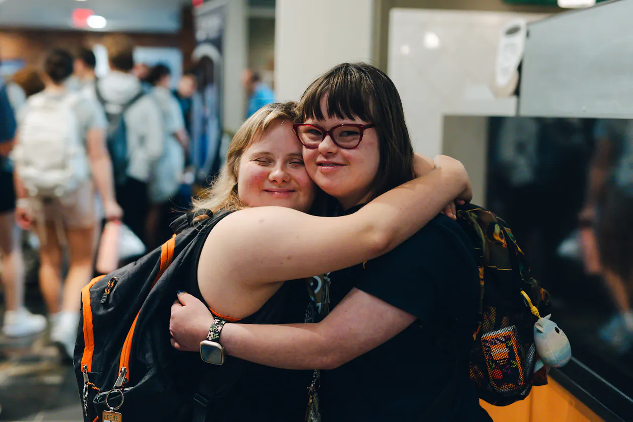 Two students with backpacks smile and hug during the BUILDing the Future: 10 Years of Impact event at Bethel.