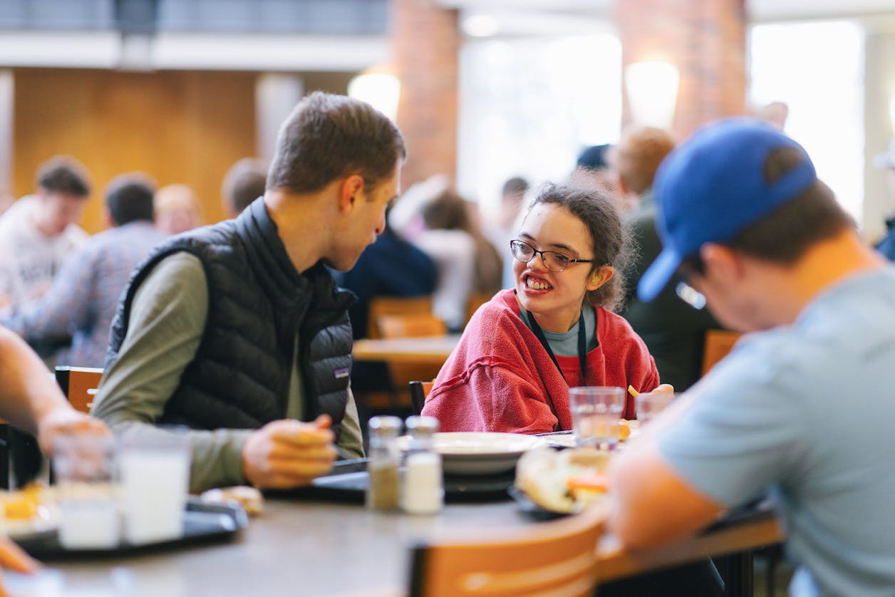 Two students in BUILD chat over lunch in a busy dining area.