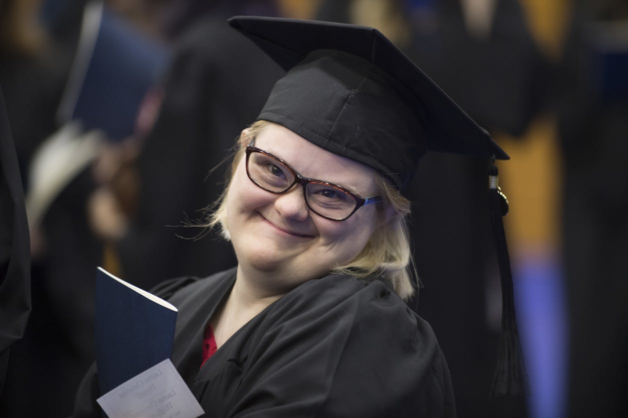 Student in BUILD smiles in a cap and gown at a graduation ceremony.