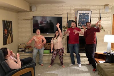 Group of friends dancing and laughing in a cozy living room while others watch and smile.
