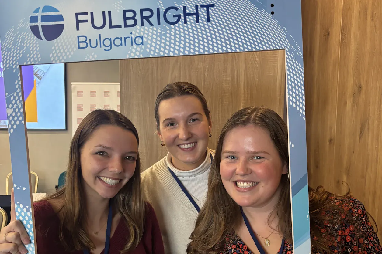 Three smiling women pose inside a Fulbright Bulgaria photo frame at an indoor event.