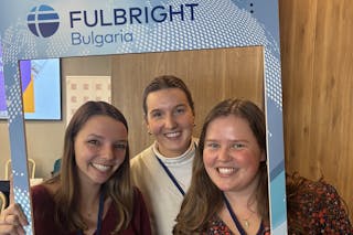 Three smiling women pose inside a Fulbright Bulgaria photo frame at an indoor event.