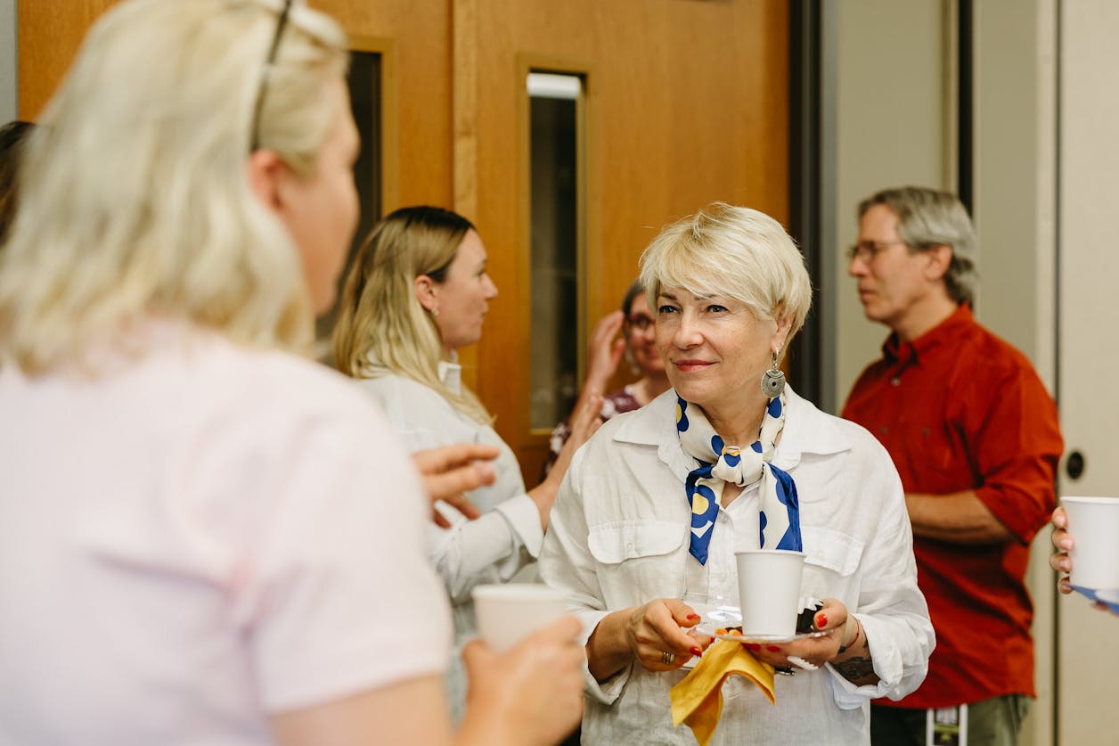 Woman smiles and chats with others while holding coffee at a campus gathering.