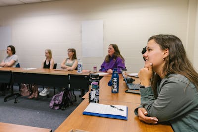 Students smiling and engaging with professor in a classroom. 