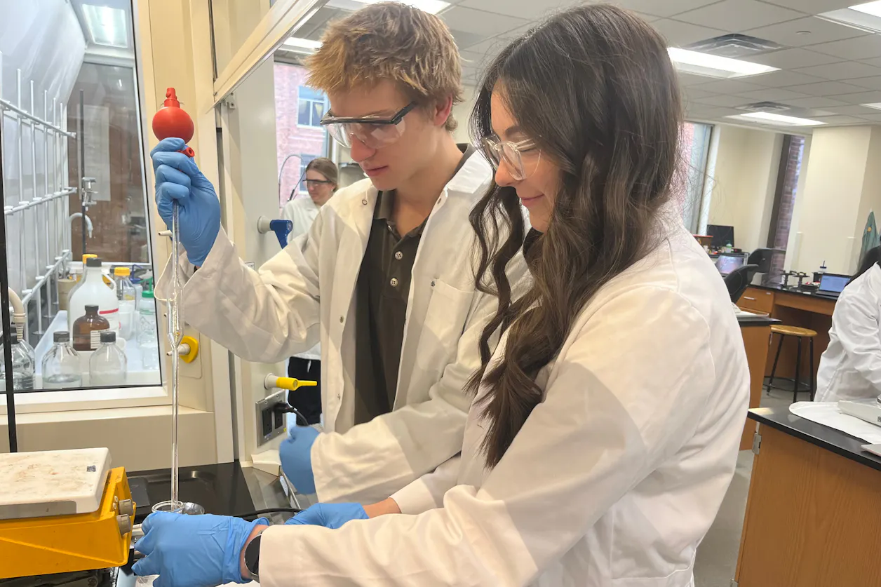 Students in white lab coats use a pipette in a chemistry lab at Bethel University