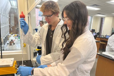 Students in white lab coats use a pipette in a chemistry lab at Bethel University