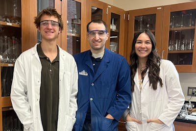 A Bethel chemistry professor and two of his students smiling in a chemistry lab