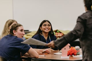 A Scrubs Camp student at Bethel University smiles during a hands-on learning session, surrounded by classmates and medical models.