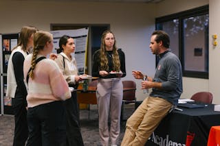 Group of students talks with a representative at an education event booth indoors.