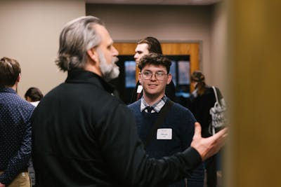 Student named Micah listens attentively during a conversation at an indoor networking event.