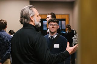Student named Micah listens attentively during a conversation at an indoor networking event.