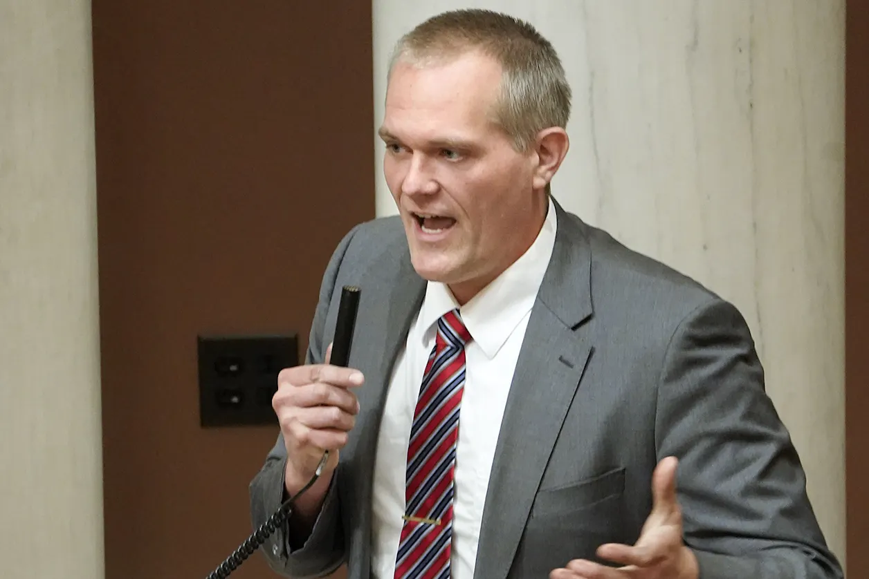 Man in a suit speaks into a microphone on the Minnesota House floor.