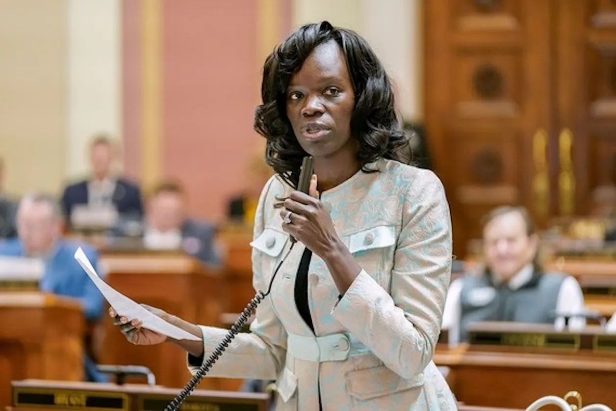 Woman speaks into a microphone while holding papers on the Minnesota House floor.
