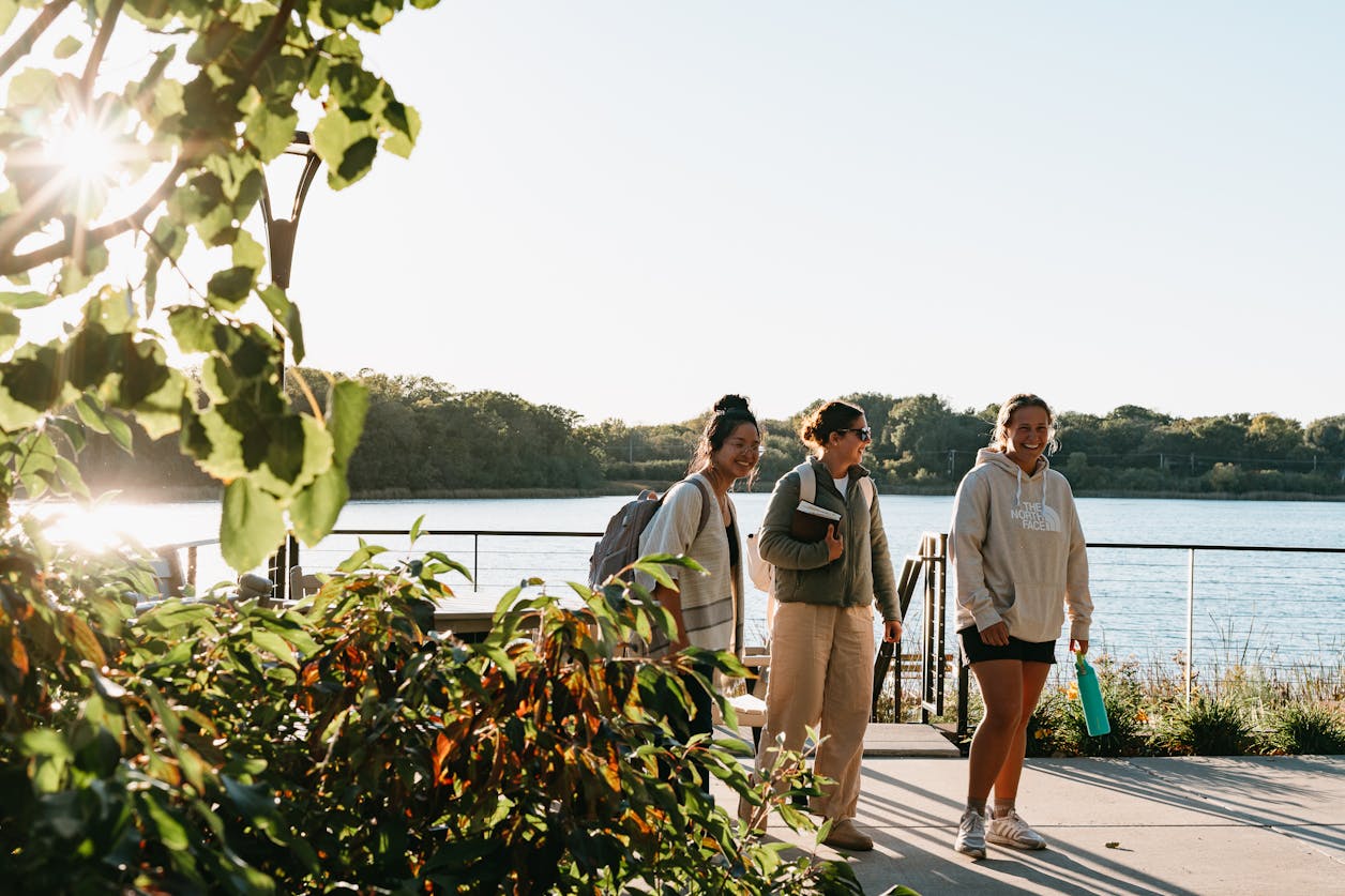 Three female students walk near Lake Valentine at sunset