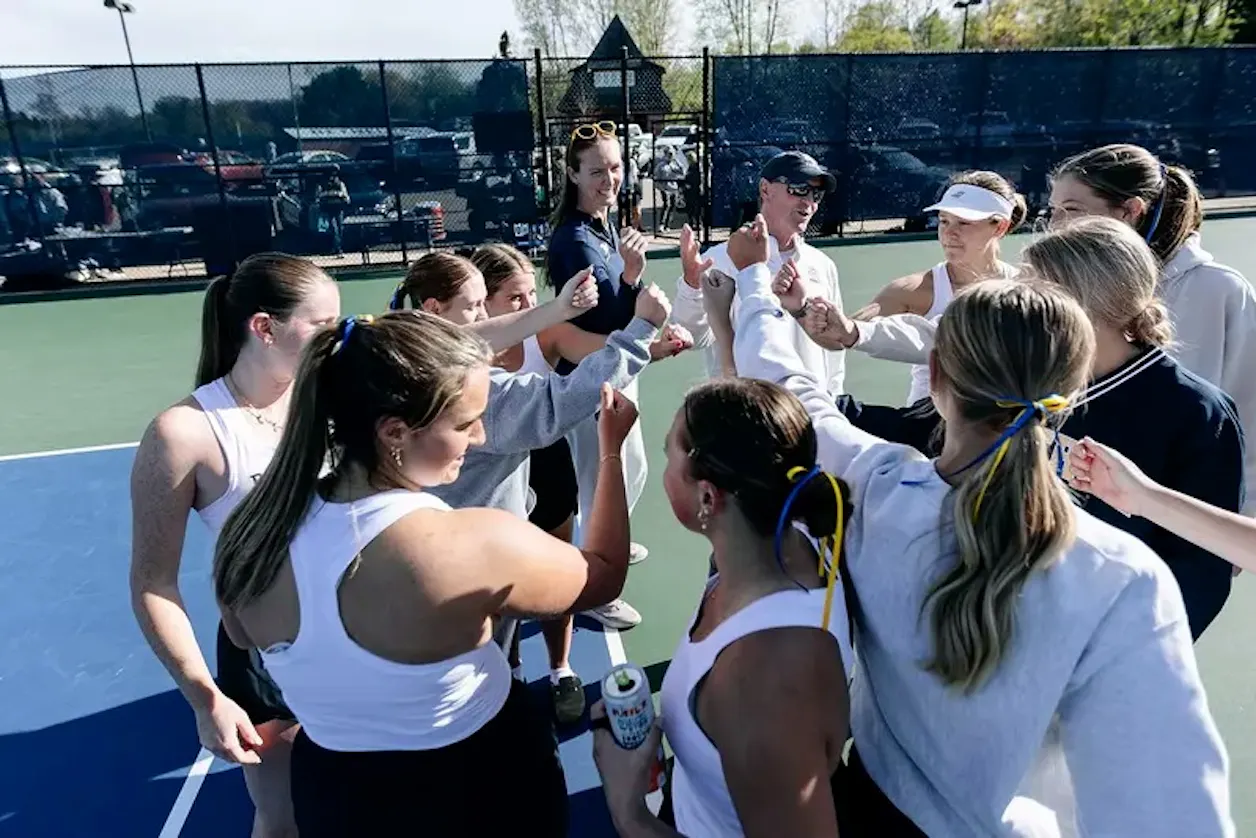 Bethel women's tennis team gathers in a pre-match huddle on the court.