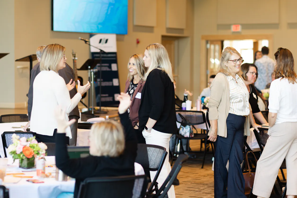 Christian EdLeaders gather around a large room and are smiling and talking with one another.