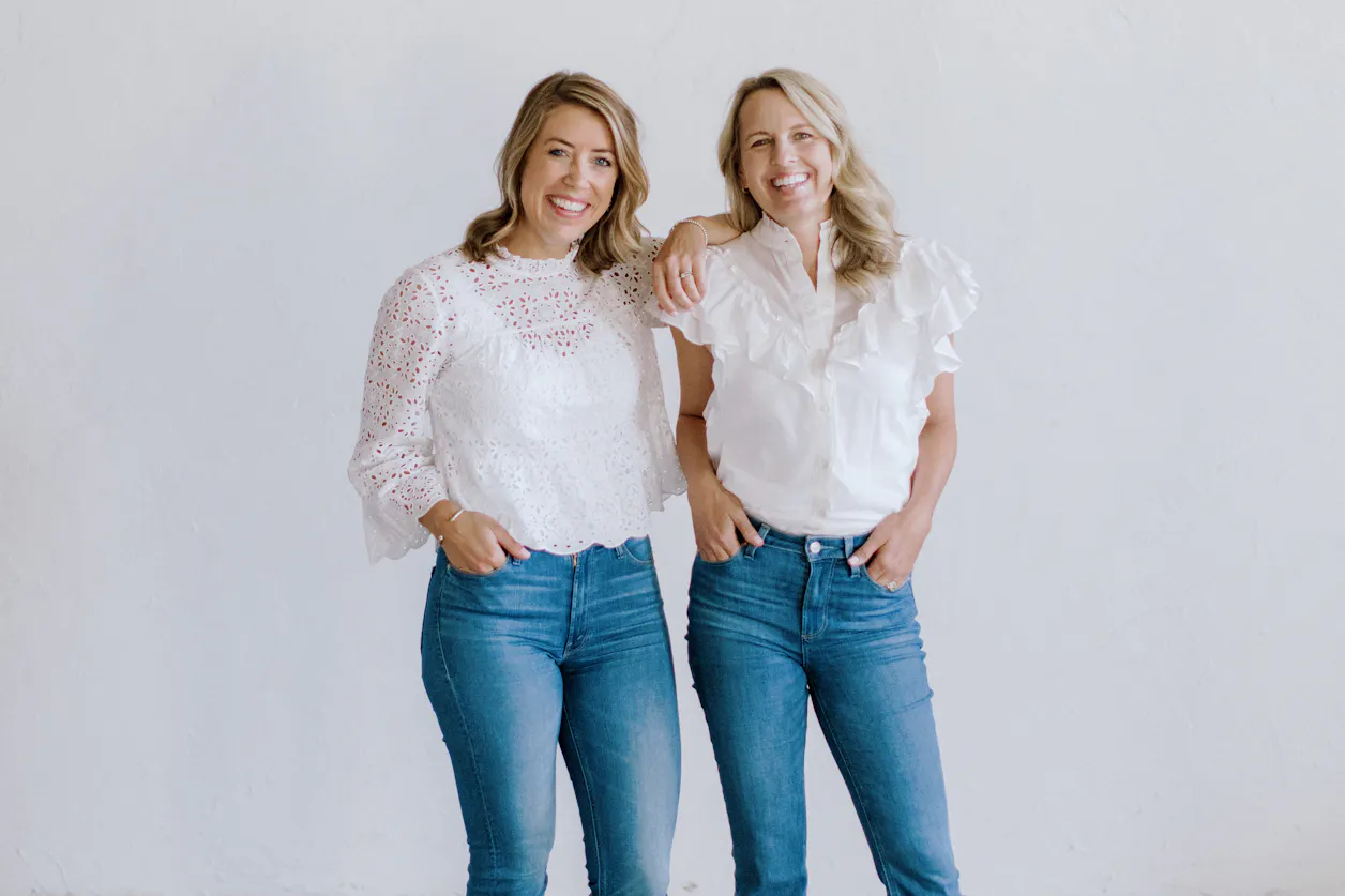 Amanda Kopischke and Angela Anderson pose together in a photography studio while wearing blue jeans and white shirts.