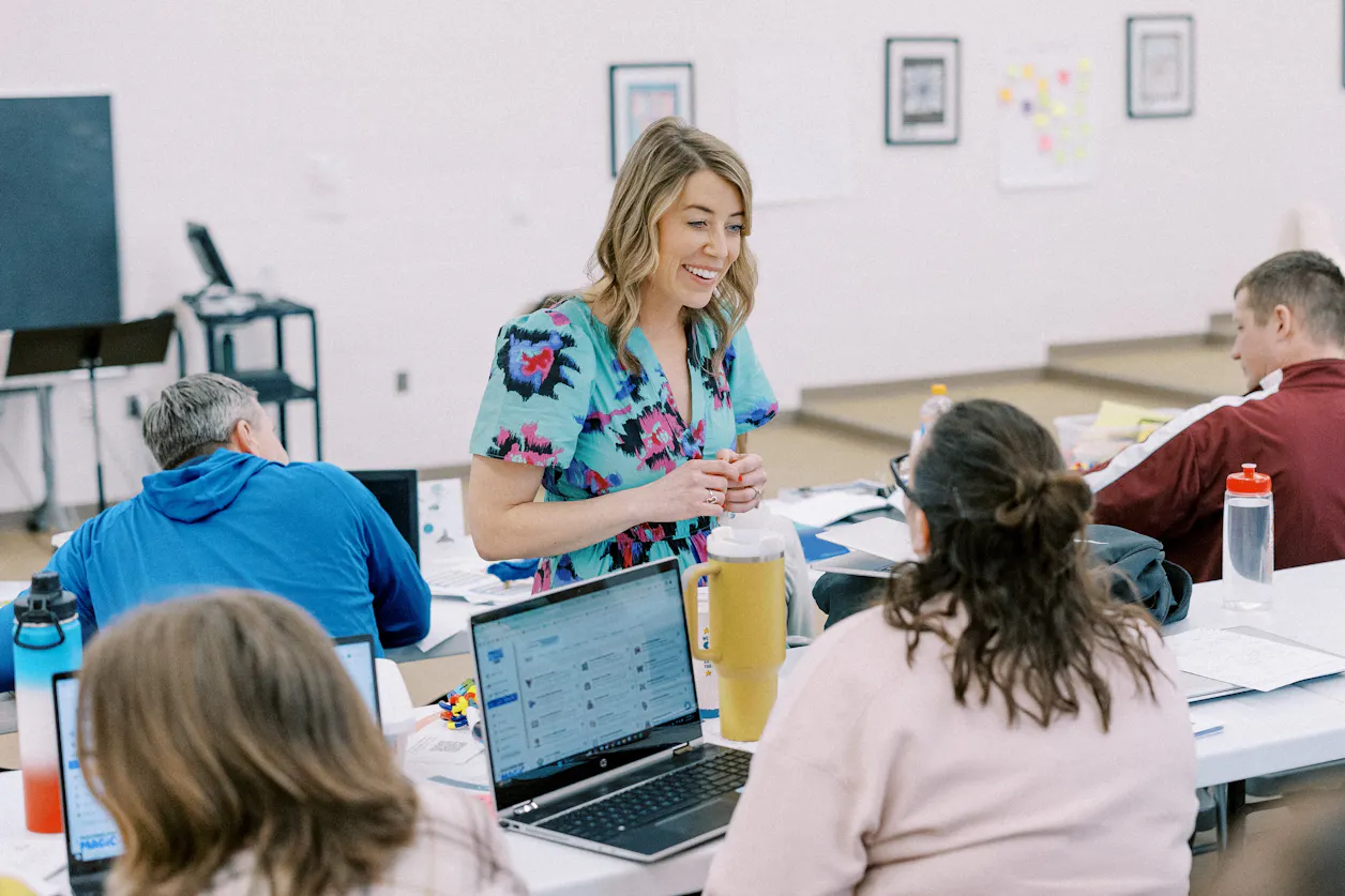 Angela Anderson ’11 GS’16 speaks to a group of educators at a table while smiling and wearing a teal floral dress.