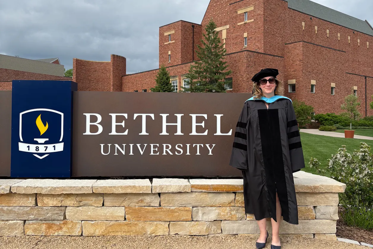 Tara Falasco '26 stands in front of the large campus Bethel University sign outside Benson Great Hall and the CLC. 