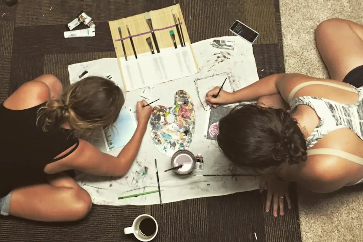 A birds-eye-view of two girls painting on a dorm room floor