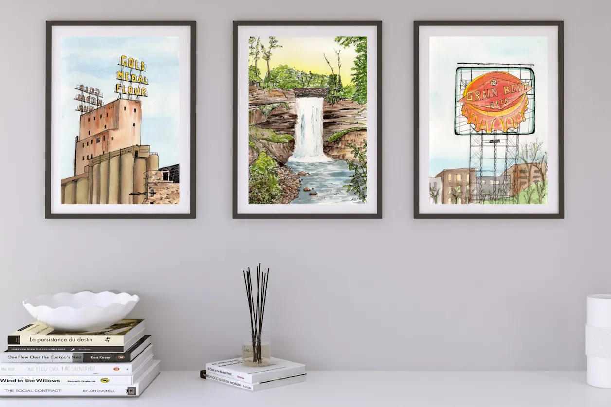 Three framed watercolor paintings created by Alyssa Whetstone '19 hang on a wall featuring three iconic Minnesota scenes - Gold Medal Flour, the Grain Belt sign, and Minnehaha Falls.