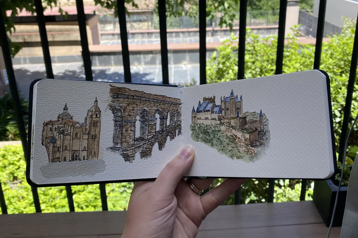 A hand holds out a sketchbook of three Spanish architecture pen drawing paintings.