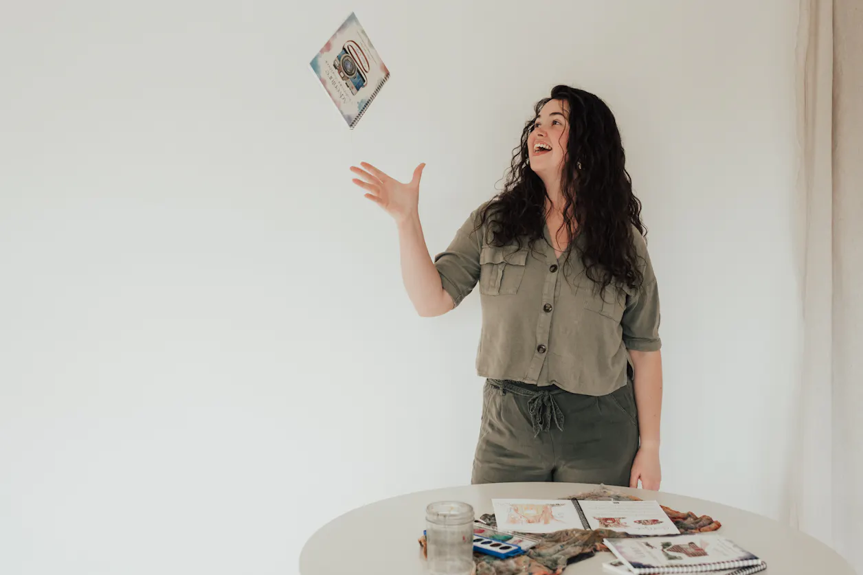 Alyssa Whetstone '19 throws her watercolor workbook in the air for a posed photo in a photography studio.