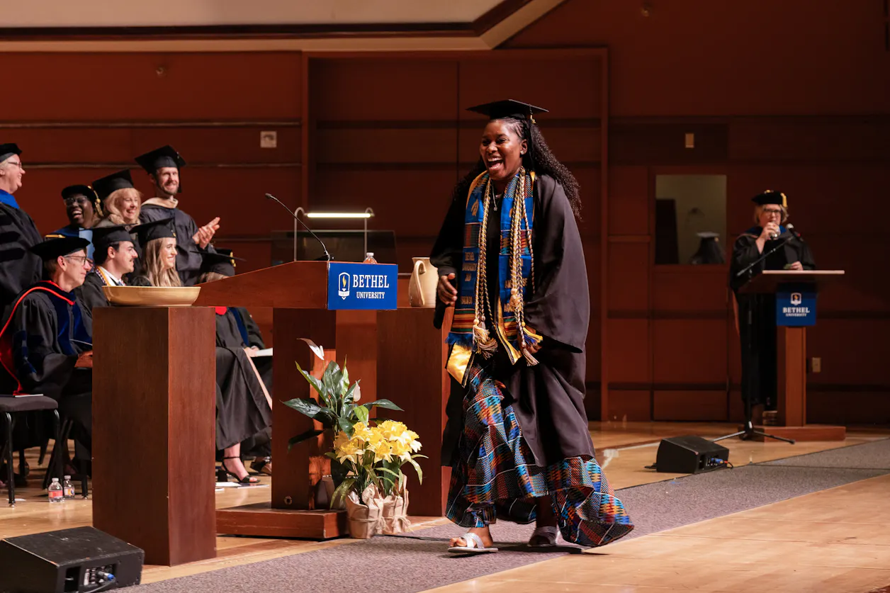 Graduate smiles while crossing the stage during Bethel University commencement ceremony.