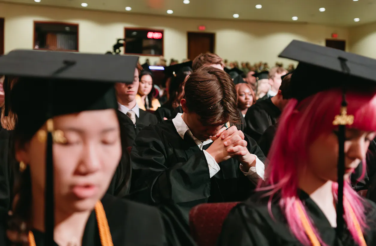 Graduates bow their heads in prayer during commencement ceremony.