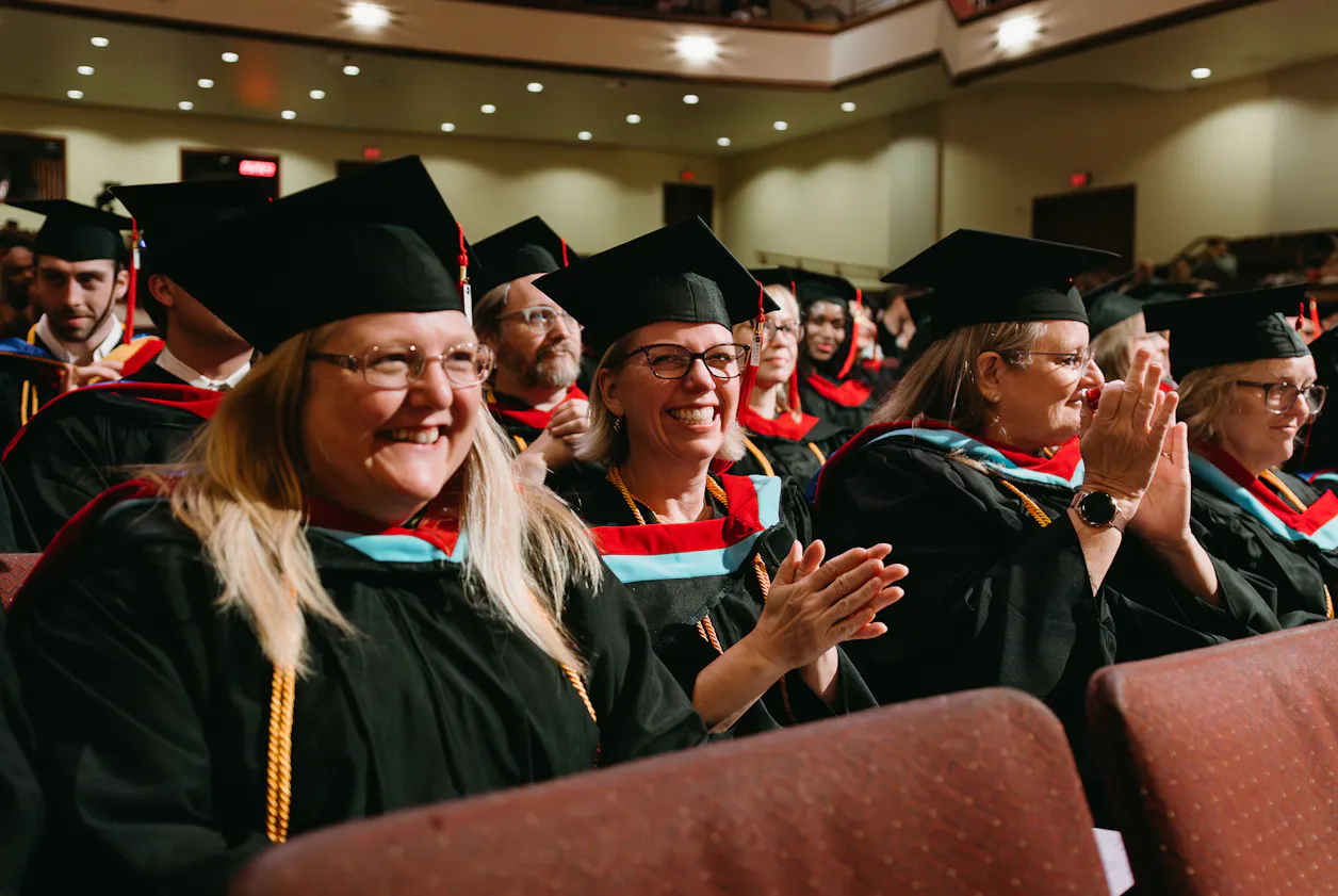 Graduates smile and applaud during commencement ceremony.