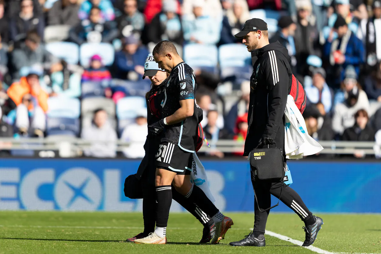 Athletic trainer Neil De Cleene assists an injured Minnesota United FC player off the field