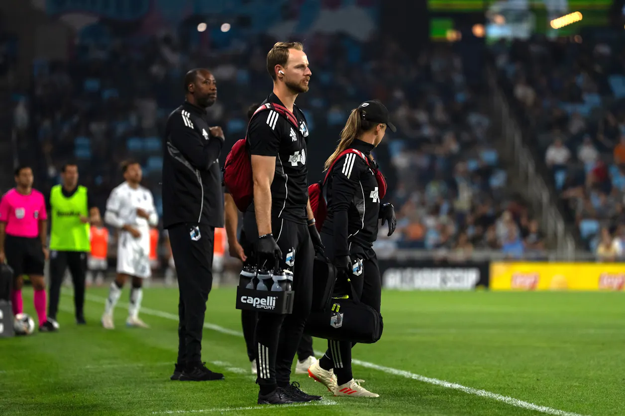 Minnesota United FC athletic trainers stand ready on the sideline during a night match